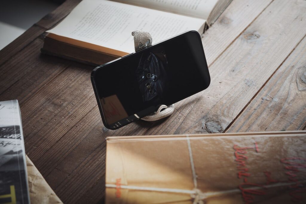 Smartphone leaning on a holder with open books on a rustic wooden table, creating a cozy ambiance.